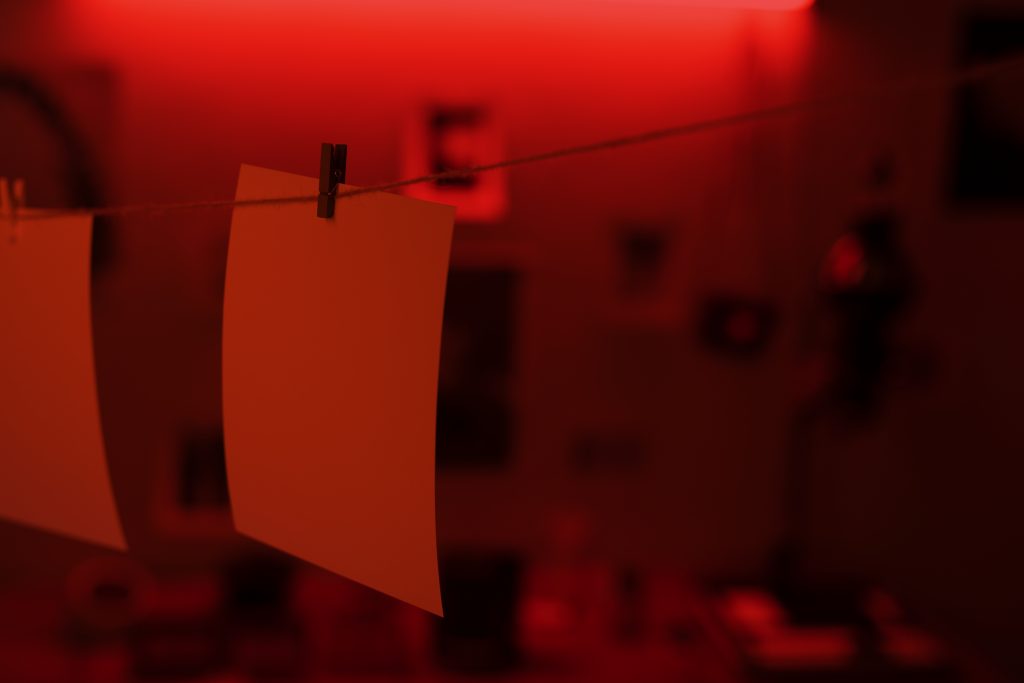 Blank evidence papers hanging on a string under red light in a darkroom — symbolizing investigation, developing crime scenes, and uncovering modern unsolved cases.

