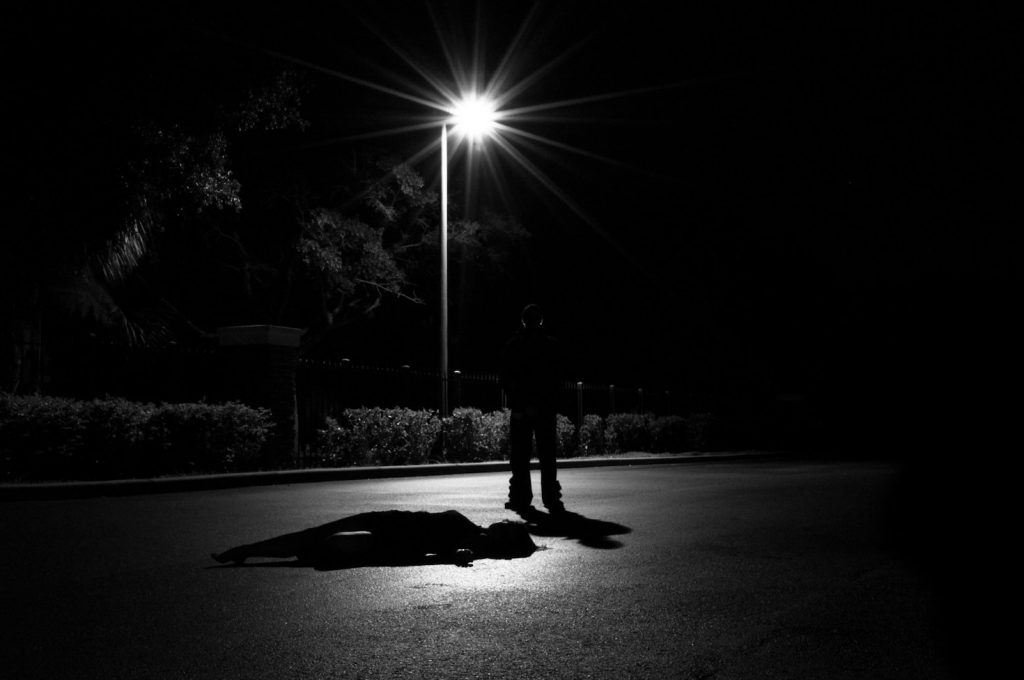 rue Crime 2025 scene showing a shadowy figure standing over a body under a streetlight, symbolizing unsolved modern crimes