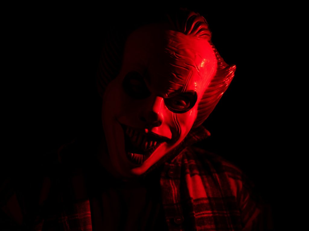 Creepy clown mask in red lighting — representing psychological horror, criminal personas, and unsettling elements in true crime storytelling.

