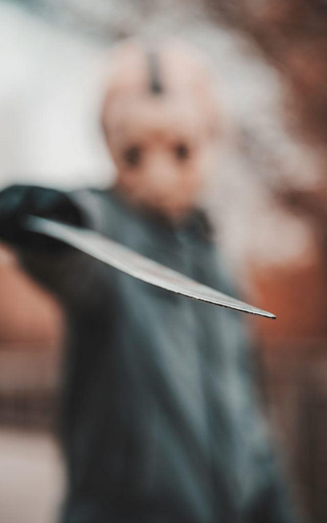 Masked figure pointing a sharp knife toward the camera — representing the chilling presence of unknown killers in true crime stories.

