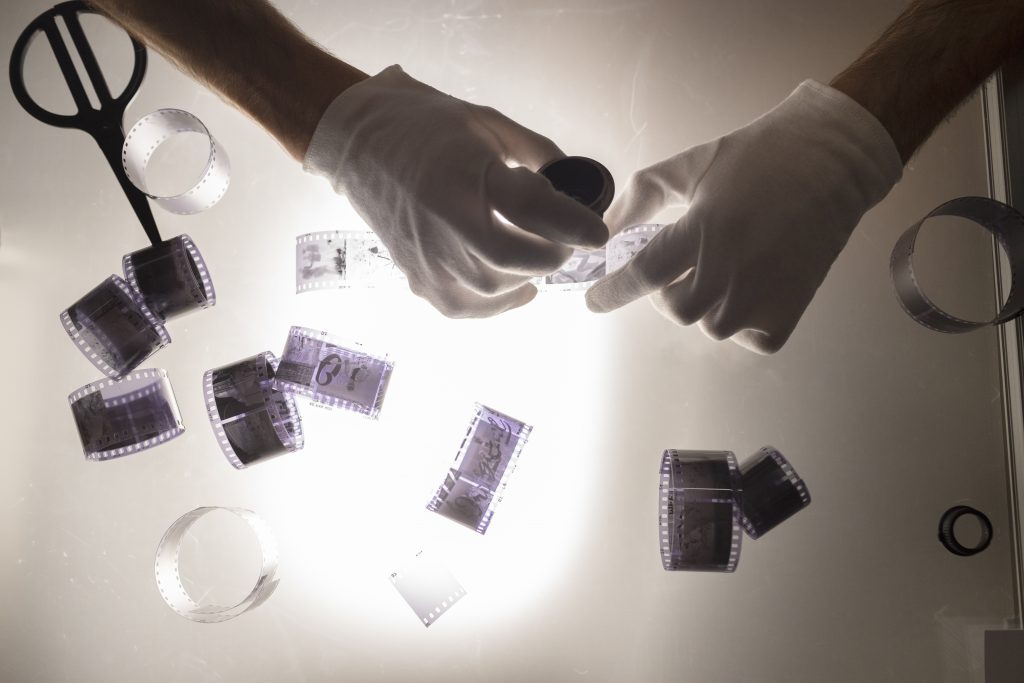 Gloved hands examining film negatives under light — exploring forensic footage and visual evidence in True Crime 2025 documentaries.

