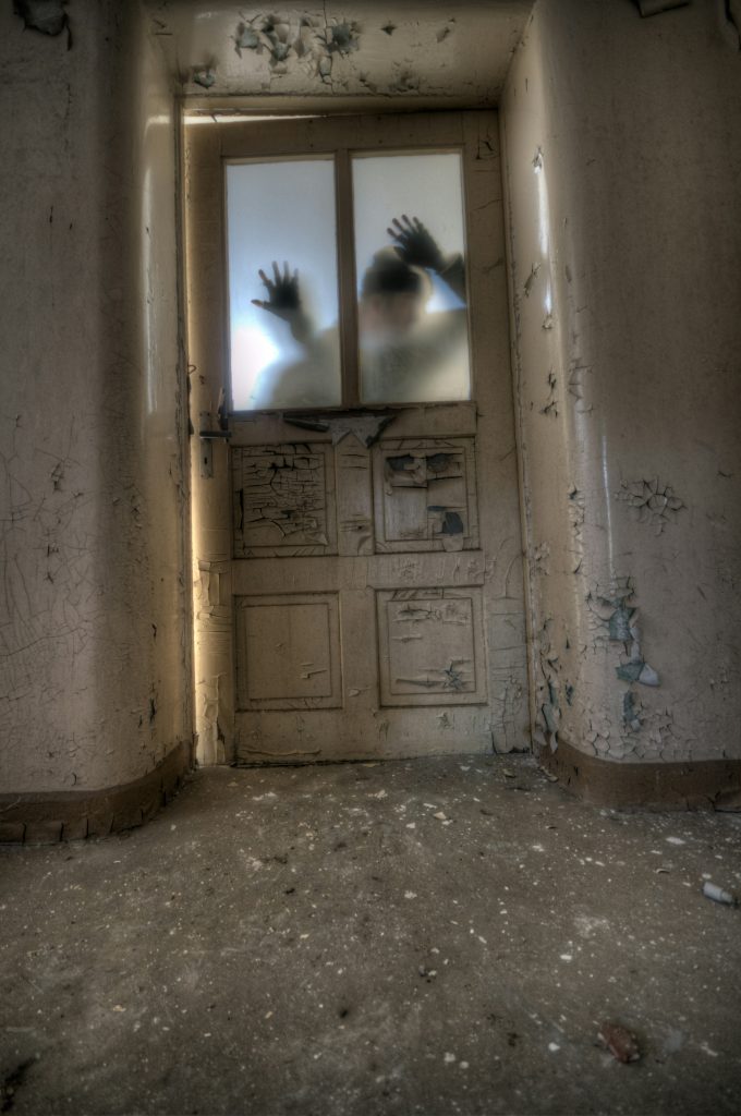 Blurred hands behind a sealed door in an abandoned building — evoking themes of captivity, horror, and unsolved crimes in true crime narratives.


